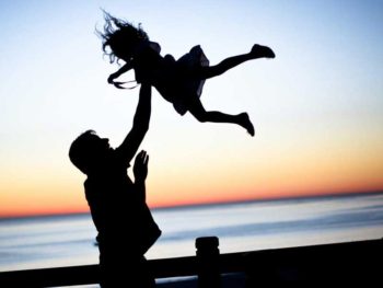 Silhouette of dad throwing daughter into air on a dock