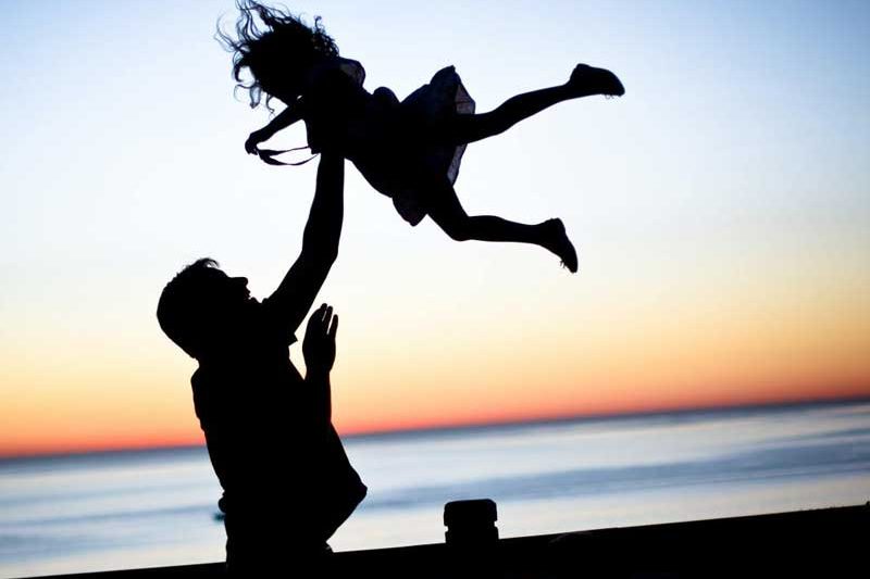 Silhouette of dad throwing daughter into air on a dock
