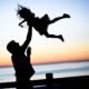 Silhouette of dad throwing daughter into air on a dock